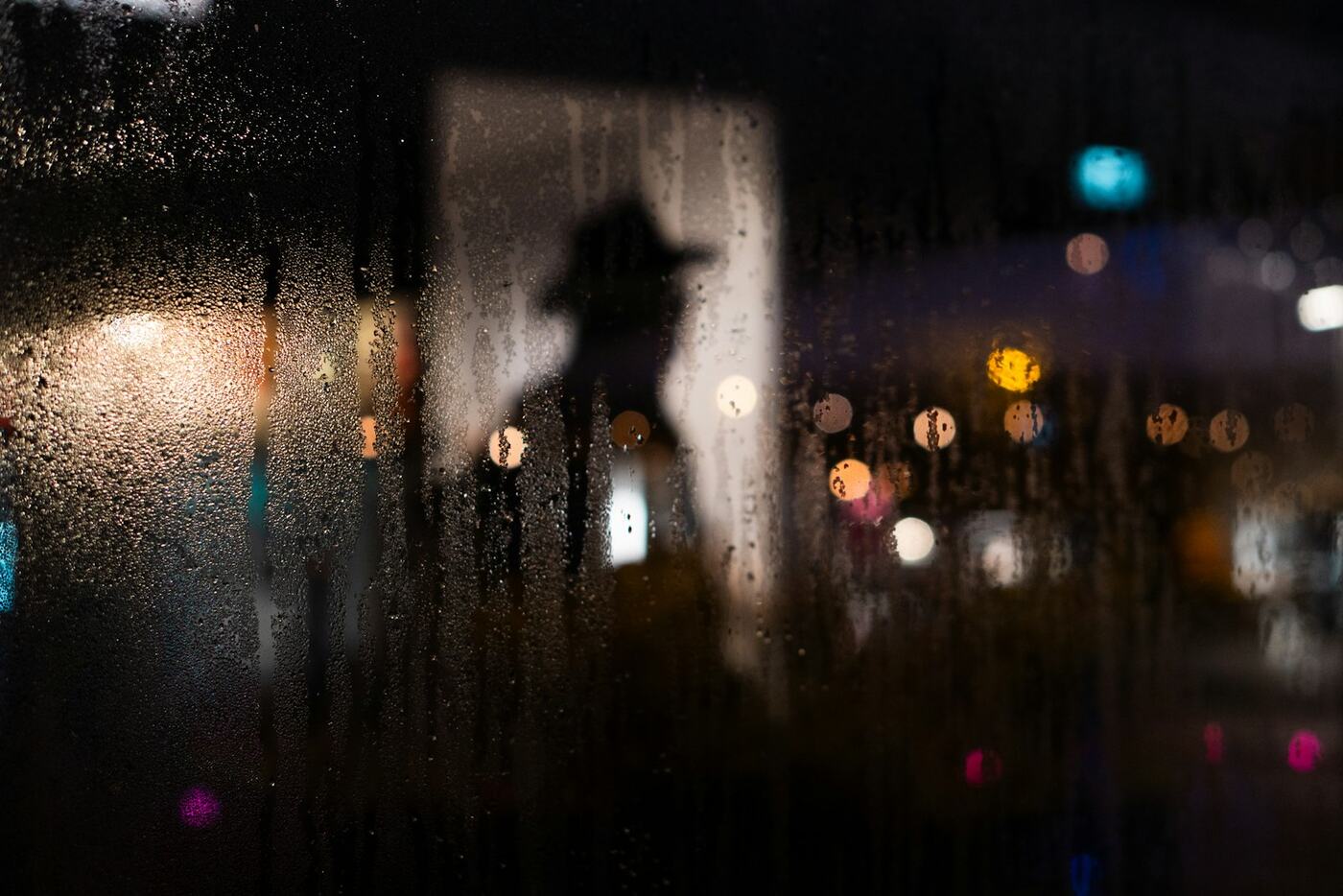 Regendruppels op een raam in het donker, met daarachter de onscherpe lichten van een straat